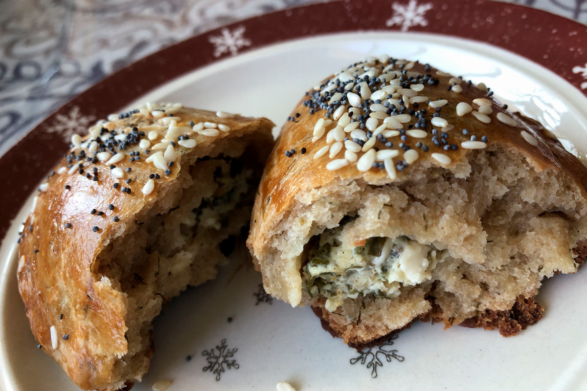 baked pastry with sesame seeds and poppy seeds on top, opened up on a plate with a cheese filling inside