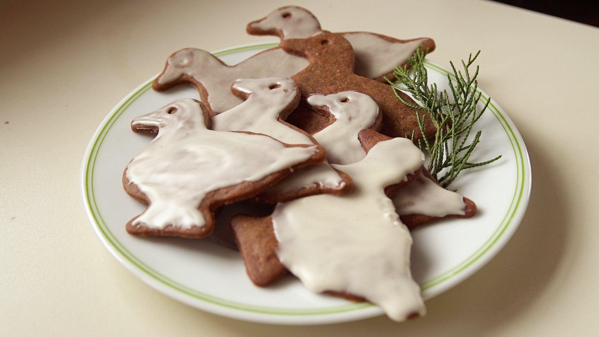 brown cookies shaped as ducks with white glaze arranged on a white plate with a sprig of pine