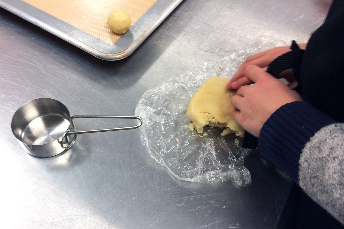 Small hands with a slab of dough and a ball of dough on a cookie sheet