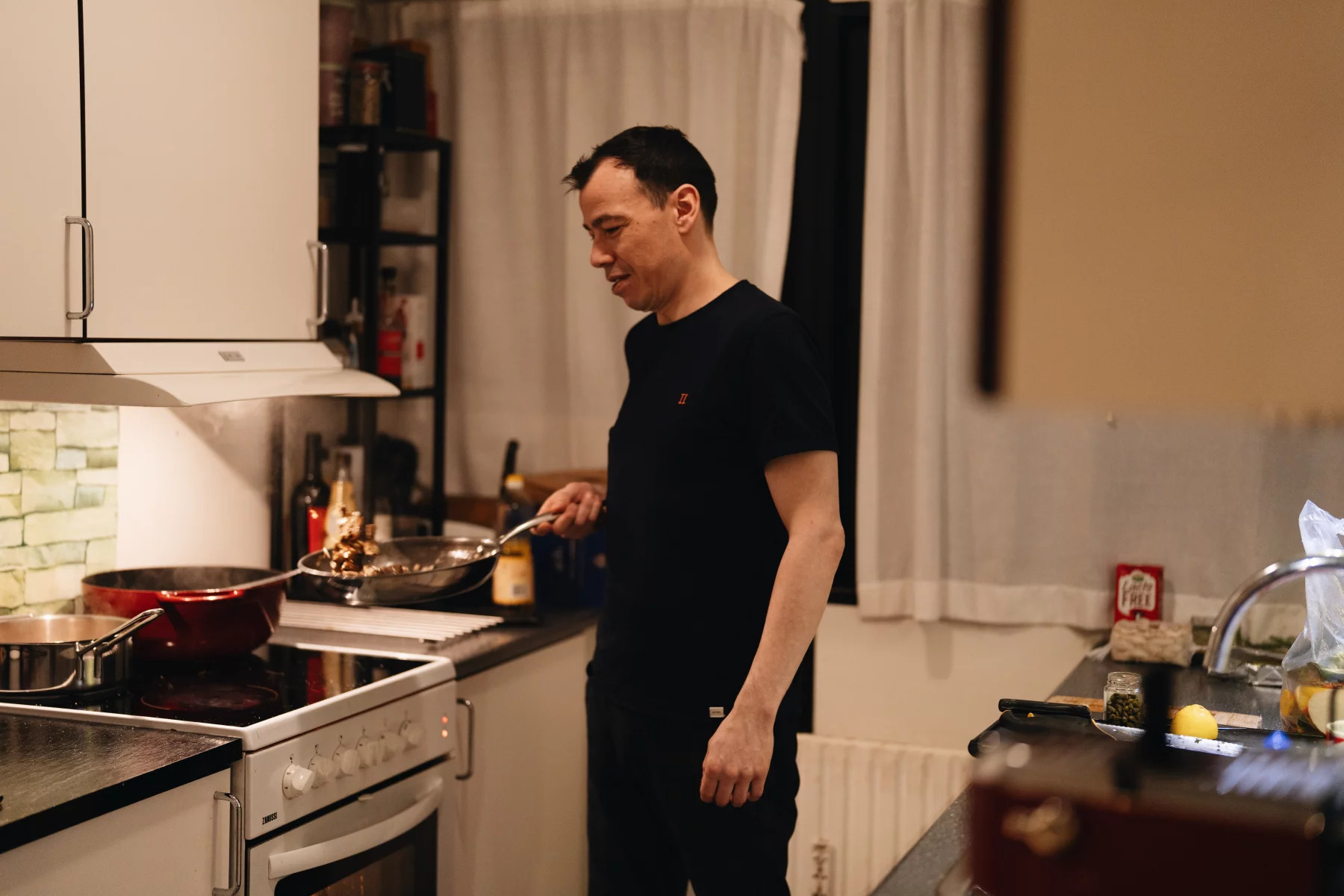 man stands over stove with pan in his hand cooking