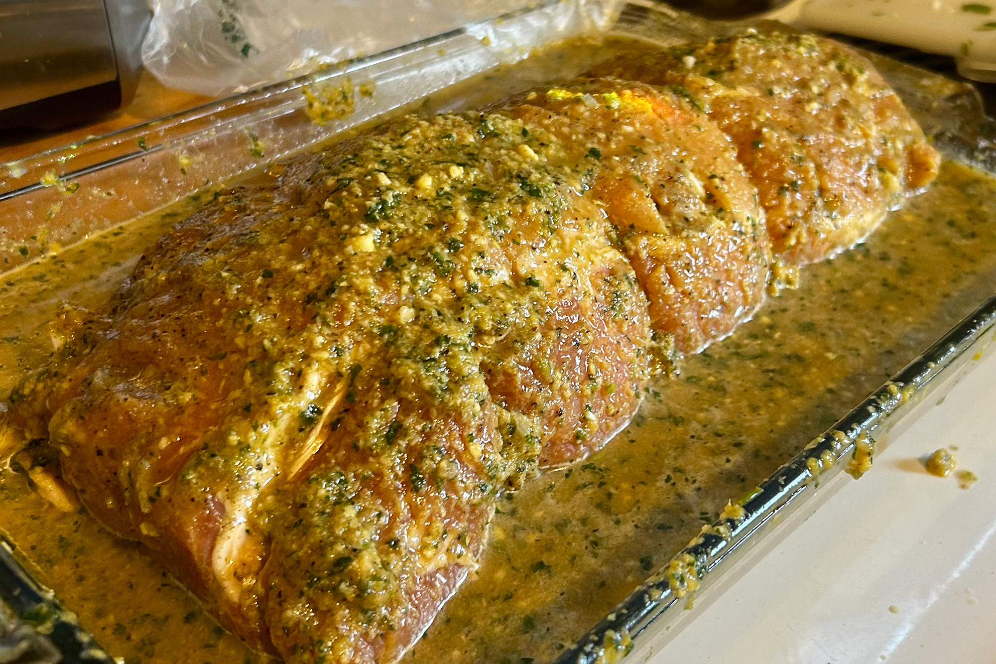 A piece of pork shoulder covered in garlic and a marinade placed in a glass pan surrounded by mojo liquid. 