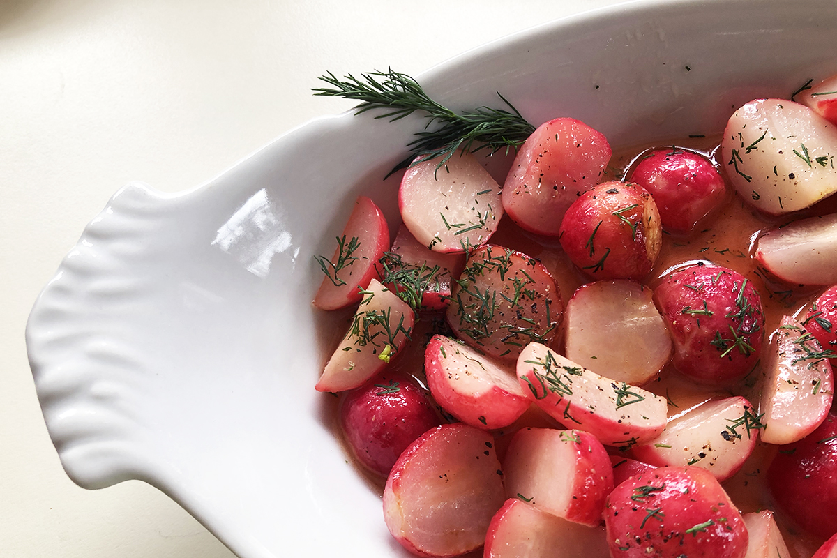 Cut pink and white radishes with herbs sprinkled on top in a white dish.