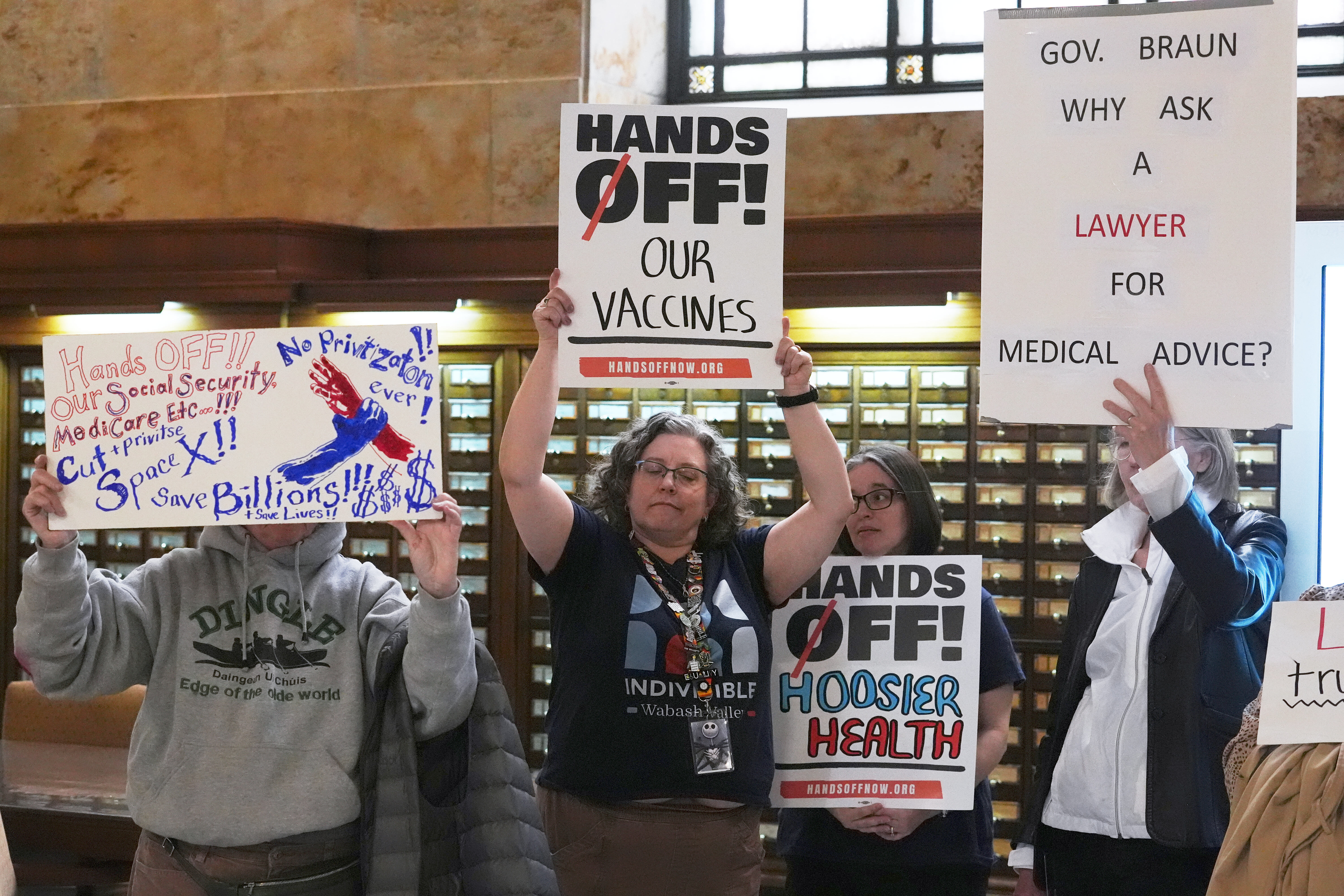 AP OK Protesters hold up signs outside of the Make Indiana Healthy Again initiative event in Indianapolis, Tuesday, April 15, 2025.