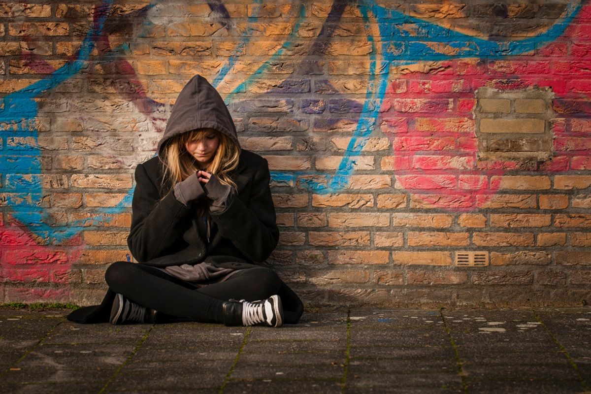 runaway girl sits in front of a wall with graffiti