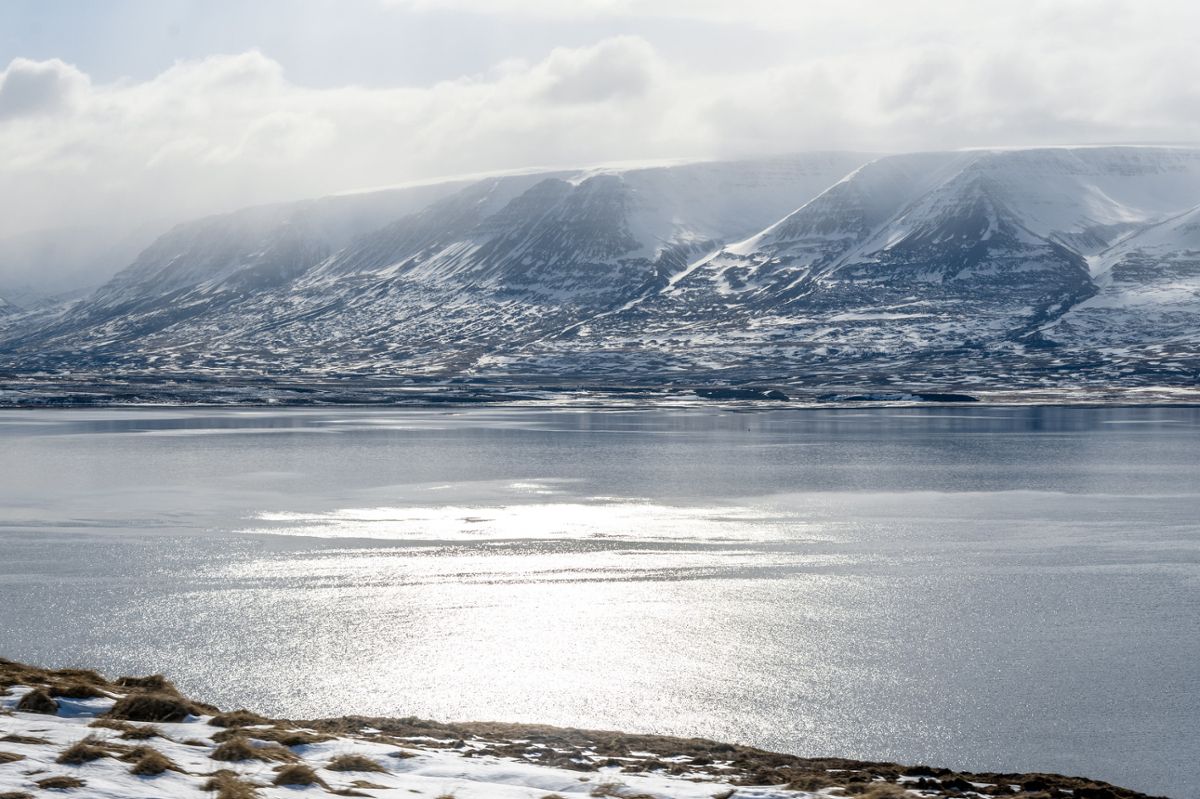 Iceland's mountainous region descending into the water with clear skies behind.