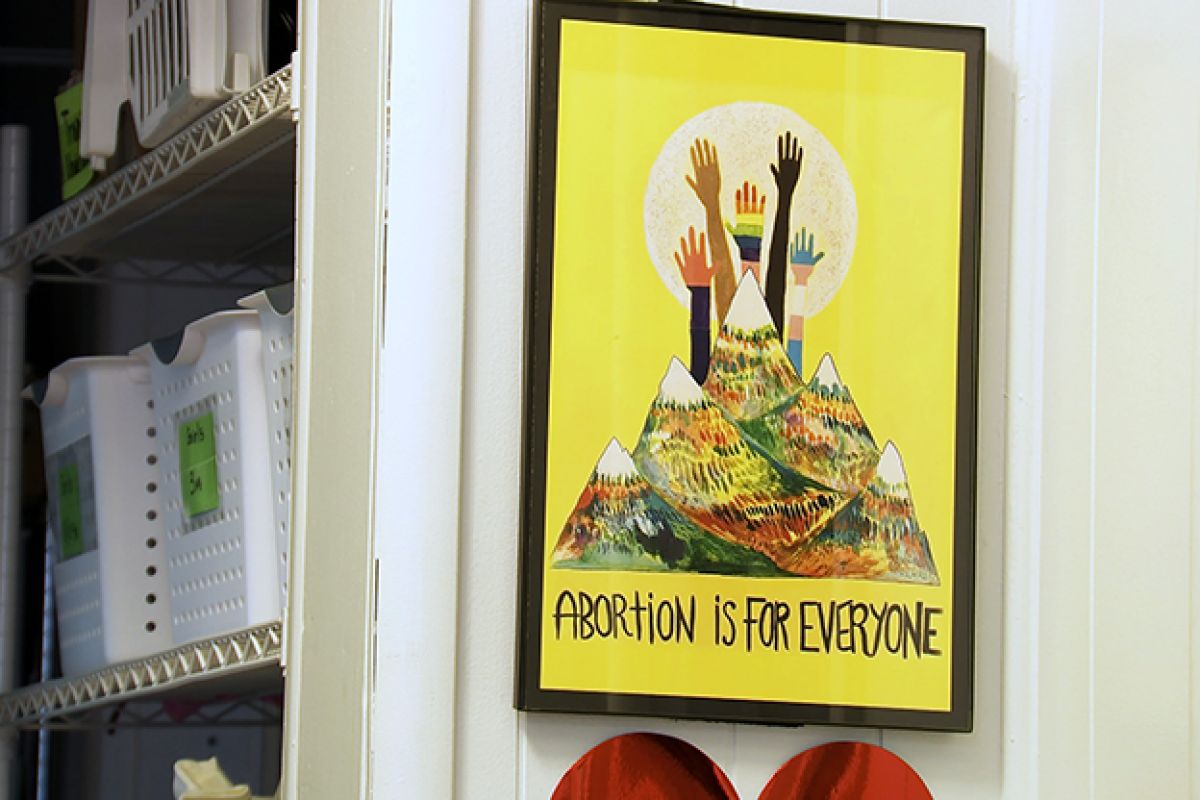 Image of a yellow image with mountains, hands and the words "abortion is for everyone"