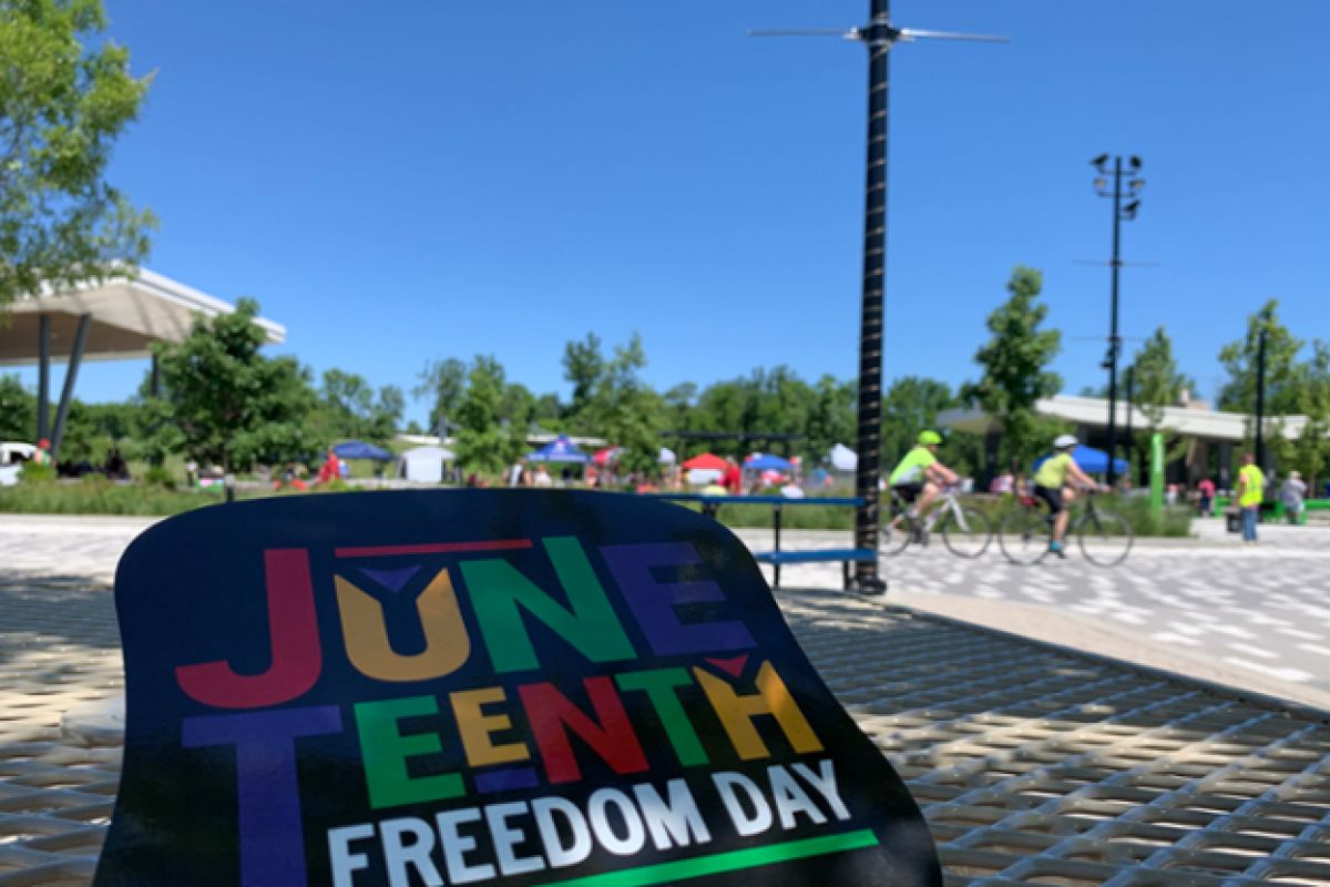 A hand fan reading "Juneteenth Freedom Day" sits on a Switchyarf Park picnic table.