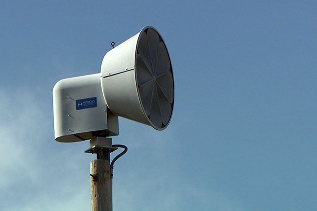 Image of a tornado siren in front of a blue sky