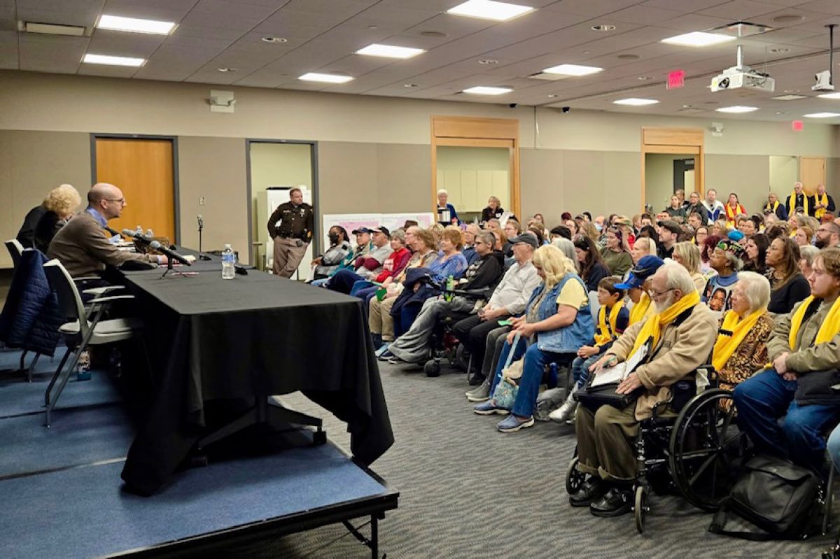 Republican Senators Vaneta Becker and Jim Tomes sit at table on the left of the image with the event's moderator. The right is a crowd of their constituents in seats in a conference space at the Evansville Vanderburgh Public Library.