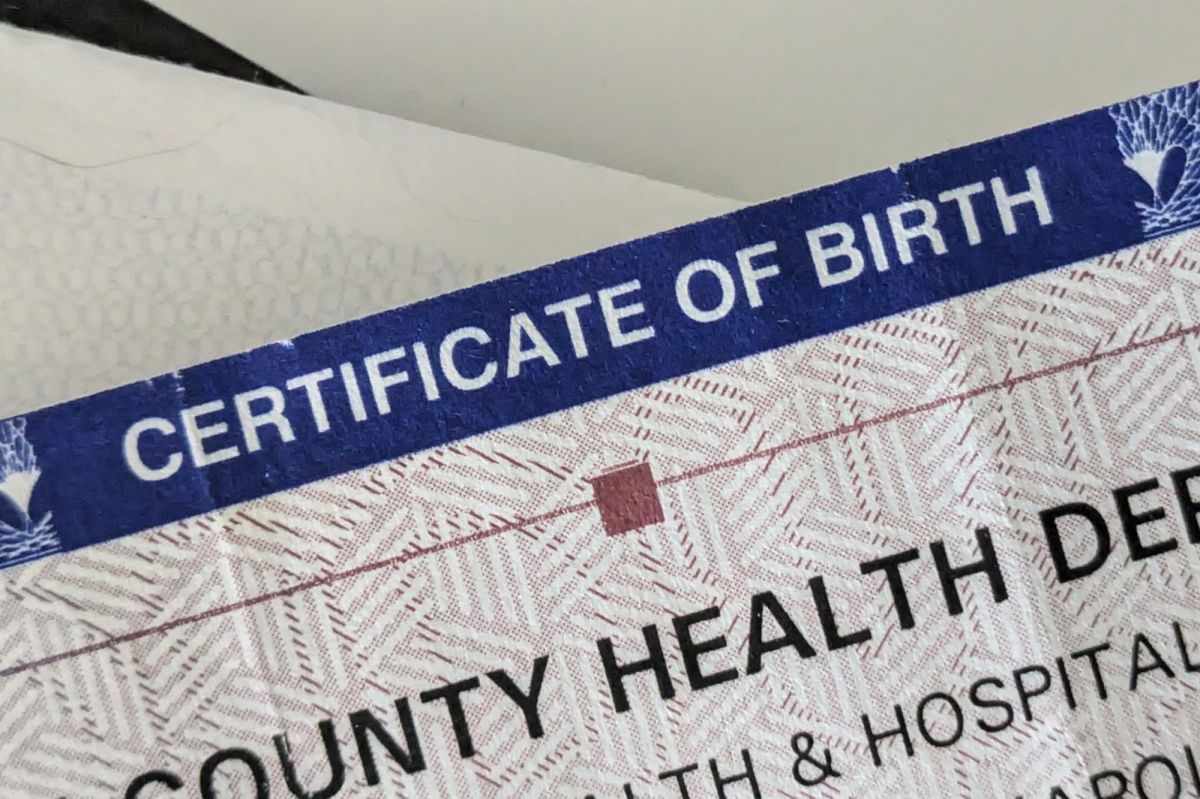 A tightly zoomed in on birth certificate. It is placed on top of a stack of other papers and in a blue border at the top is written "CERTIFICATE OF BIRTH."