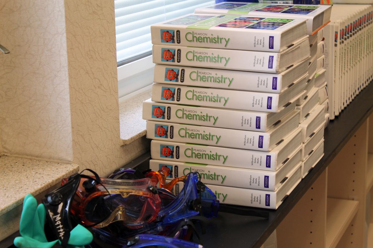 A stack of chemistry books and goggles sit on a window ledge in a classroom.