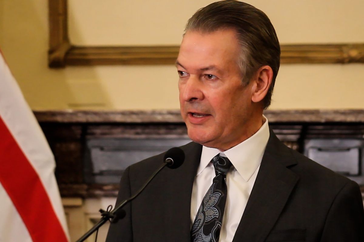 David Adams stands at a microphone in the governor's office. He wears a suit and tie. To the left is an American flag that is cut off in the image.