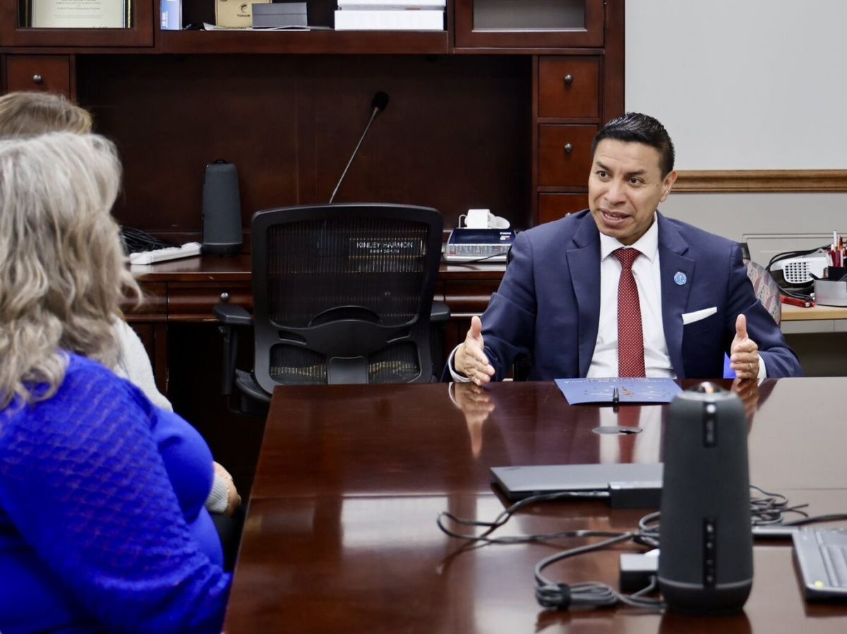 secretary of state sitting at desk talking to two people