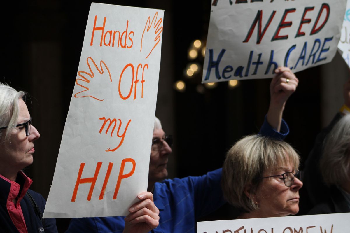 People gathered at a rally holding signs. One person holds a sign that reads "Hands off my HIP."