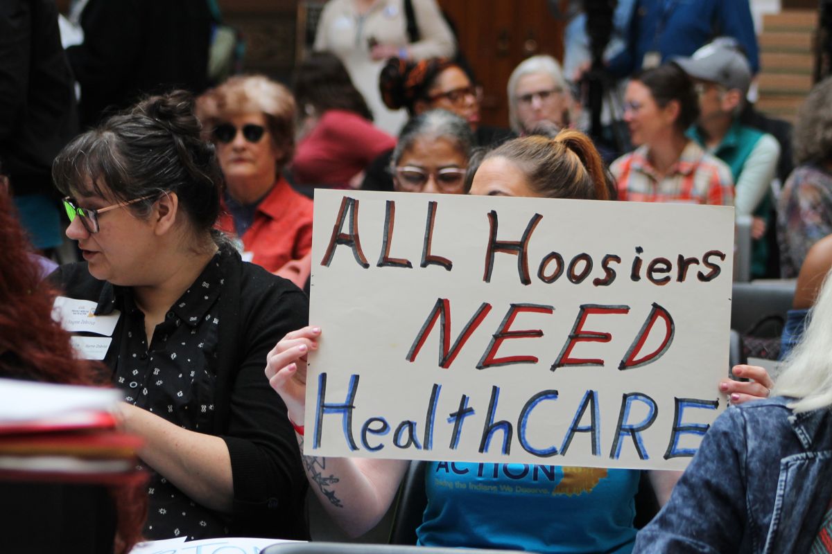 A person at a rally holding a sign that says "All Hoosiers need health care."