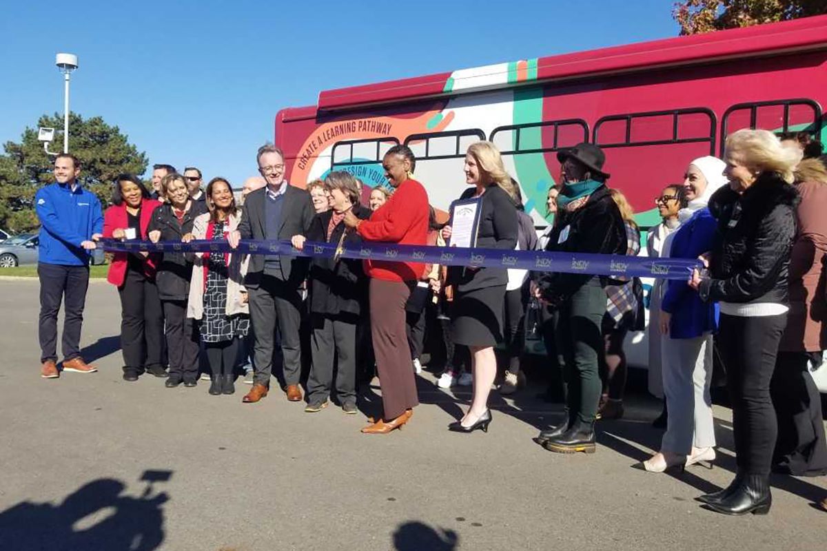 Indiana Wesleyan University staff and community partners stand in front of a colorful miniature "mobile career lab" bus for a ribbon cutting on November 2, 2023.