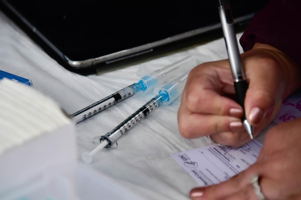 syringes and someone filling out vaccine card