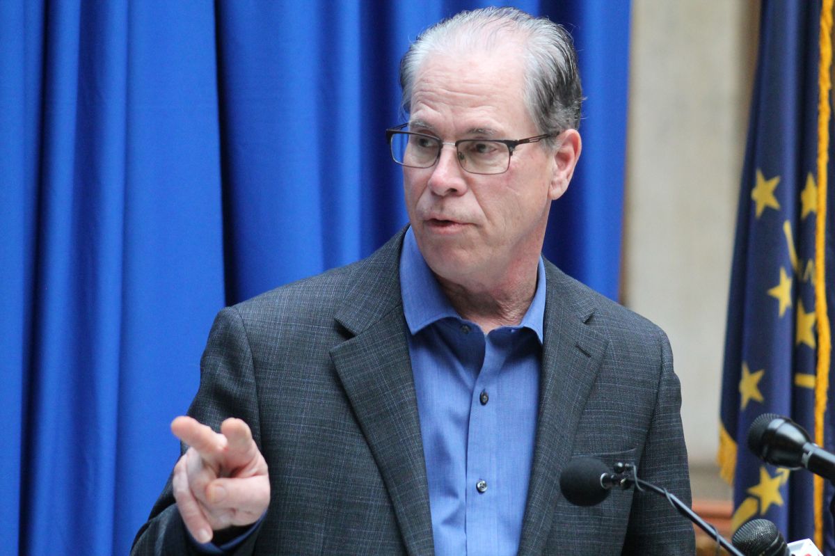 Mike Braun gestures as he speaks at a lectern. Braun is a White man, balding with gray hair. He is wearing a suit.