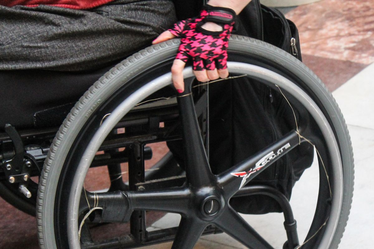 A person using a mobility aid, rolling their wheelchair in a pair of black and pink houndstooth patterned gloves.