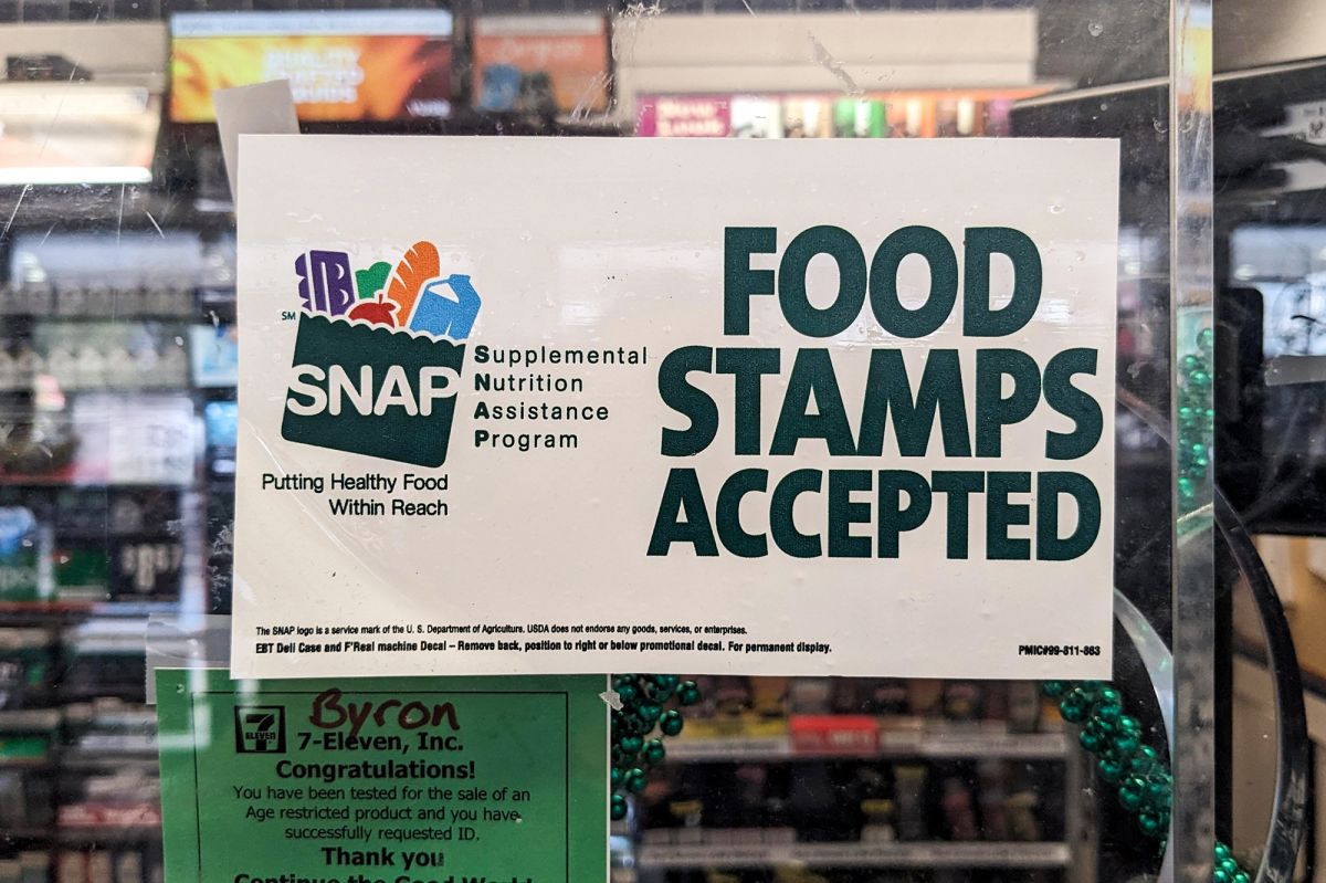 A sign at a grocery store has the SNAP logo on one side, while the other side reads "Food Stamps Accepted."