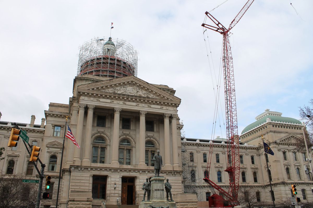 The Indiana Statehouse sits against a blue sky with a construction crane in the background.