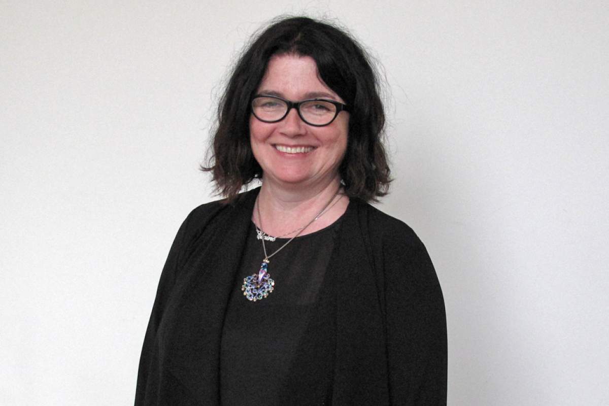 Elaine Monaghan in black sweater, glasses, wearing necklace