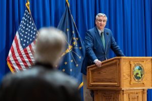 Todd Huston and Rodric Bray sit next to each other, speaking to each other. Huston is a White man with dark, graying hair. He is wearing a black suit. Bray is a White man with dark, graying hair. He is wearing a gray suit.