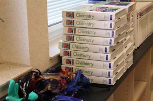 A stack of chemistry books and goggles sit on a window ledge in a classroom.