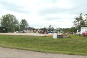 Debris is strewn across a flat landscape from where a home was demolished by a tornado. All that is left of the home is its basement. Across the street, other homes are damaged or partially collapsed. Construction equipment is parked on the street as
