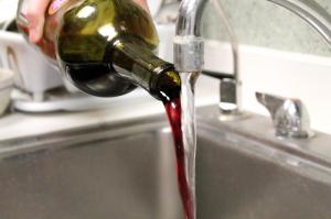 An image of someone pouring out a bottle of red wine into a sink.